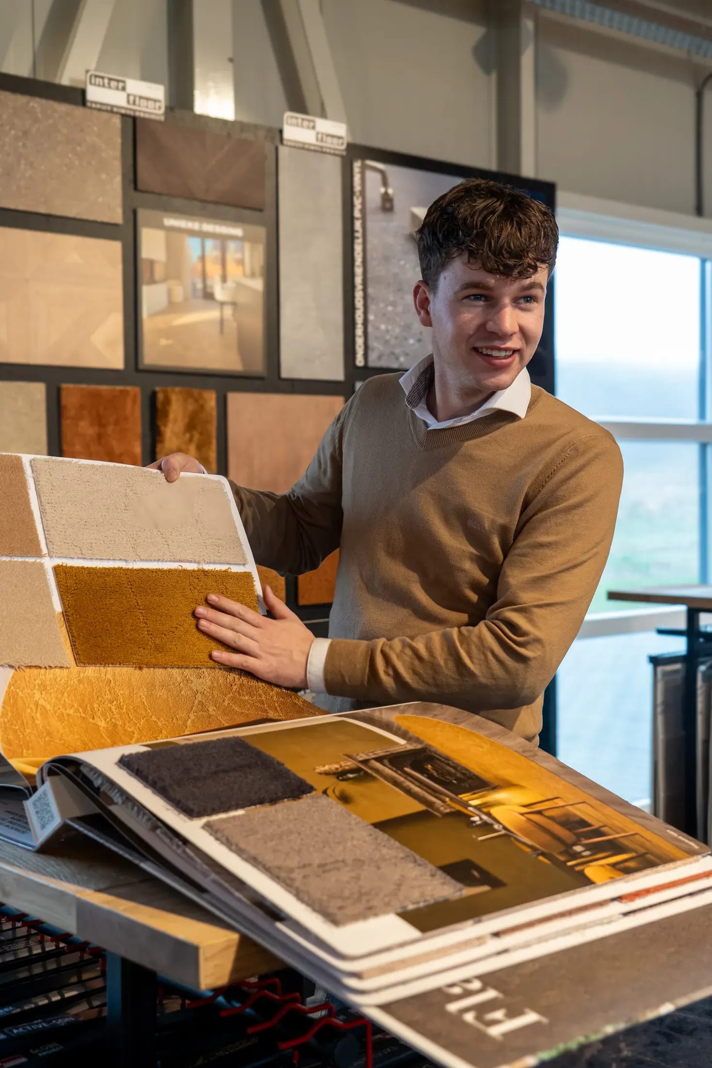 Medewerker toont tapijtstalen in oker en beige bij de stalenwand in de showroom.