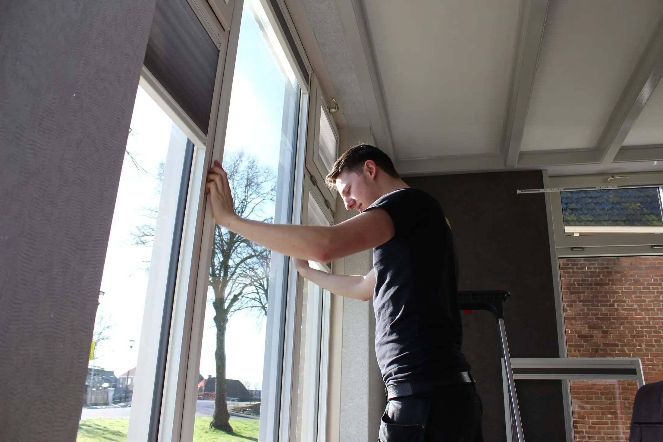 Vakman monteert een plisségordijn in het kozijn van een woonkamer.
